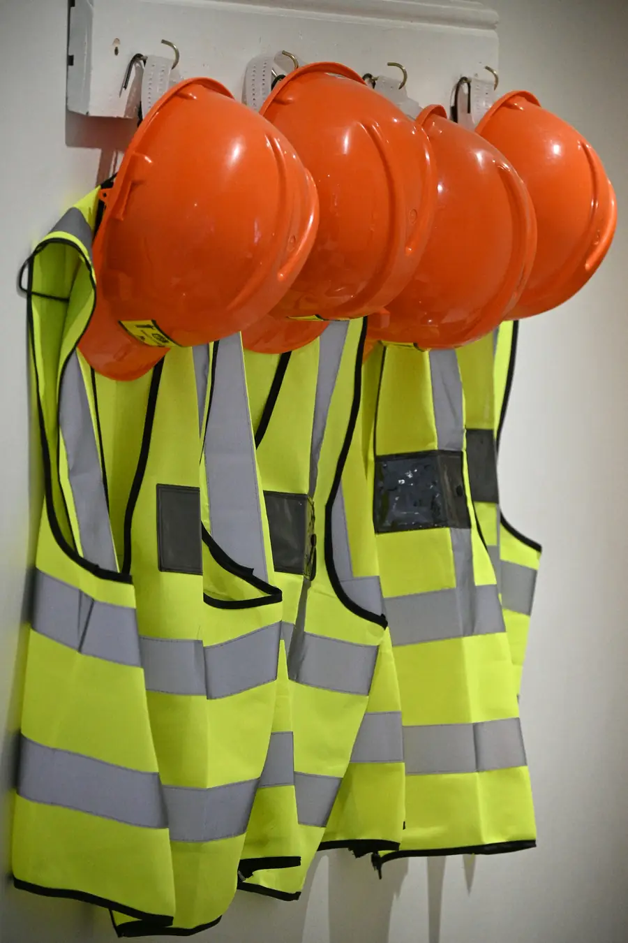 Orange hard hats and hi-vis safety vests hanging on a wall