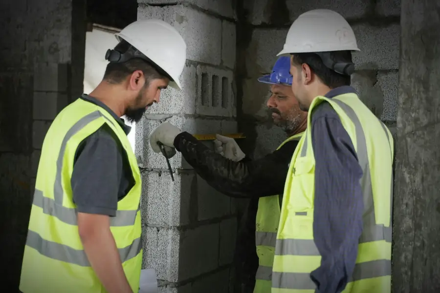 Construction workers in hard hats and hi-vis vests measuring a concrete wall on a commercial site